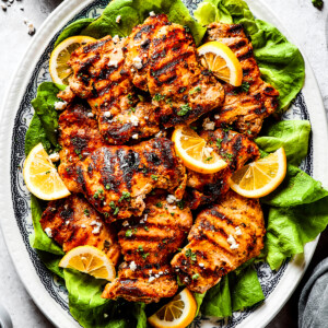 Grilled chicken thighs and lemon slices on a bed of salad greens.