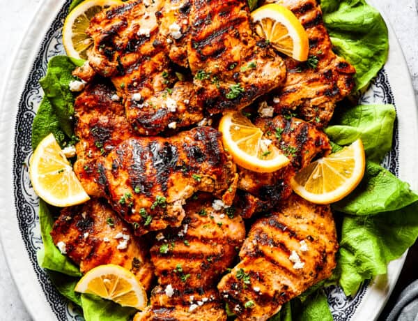 Grilled chicken thighs and lemon slices on a bed of salad greens.