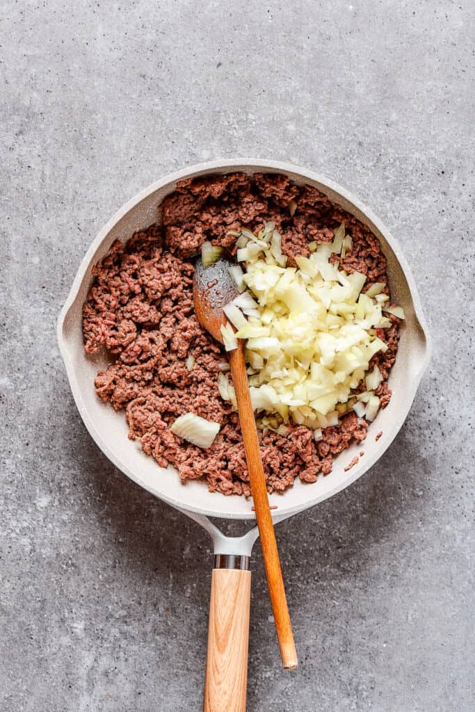 Adding onion to a skillet of ground beef.