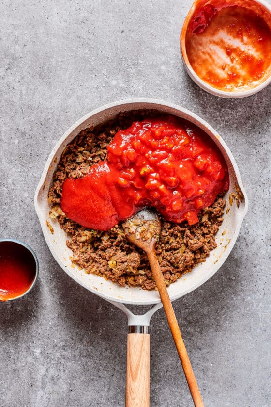 Tomato puree and diced tomatoes in a skillet with ground beef.