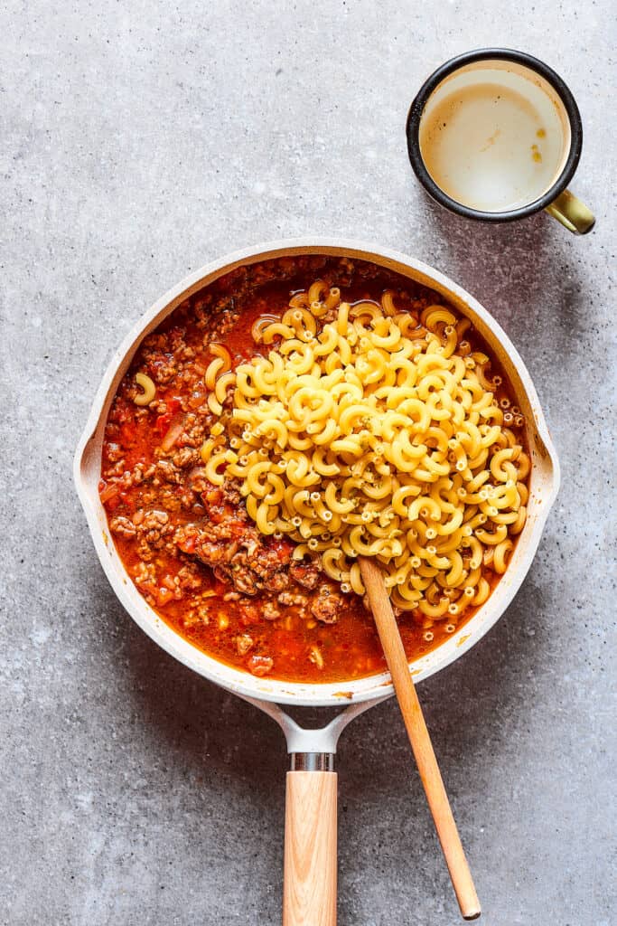 Adding macaroni pasta to a skillet of beef and sauce.