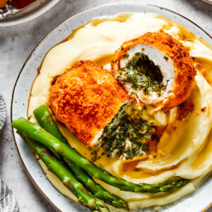A serving of mashed. potatoes and asparagus with chicken Kiev cut in half to show the buttery filling.