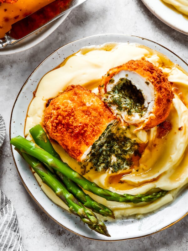 A serving of mashed. potatoes and asparagus with chicken Kiev cut in half to show the buttery filling.
