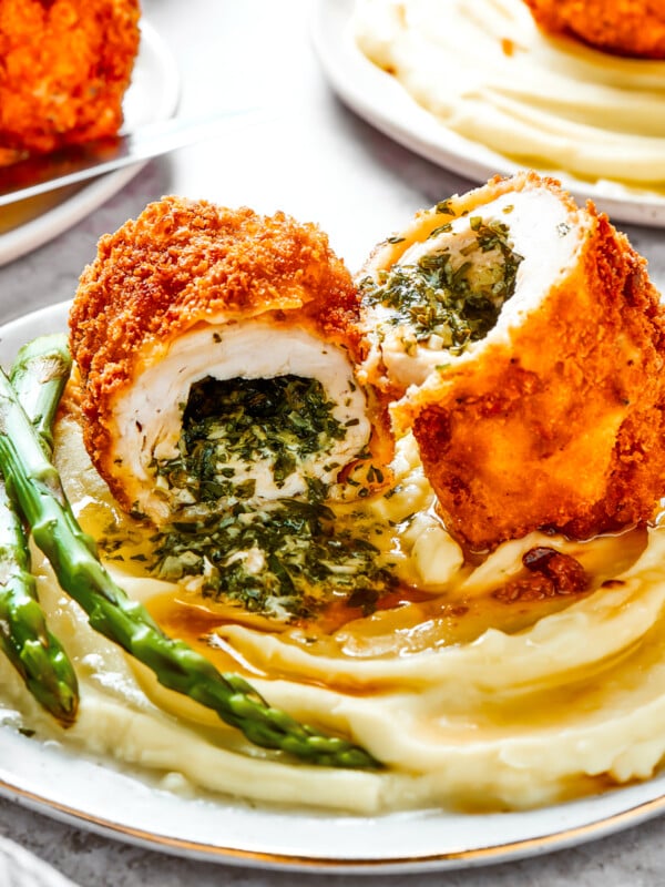 A serving of mashed. potatoes and asparagus with chicken Kiev cut in half to show the buttery filling.