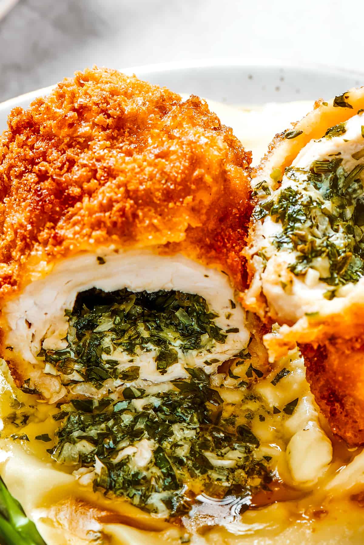 Close-up shot of cut chicken Kiev atop mashed potatoes, with garlic butter pouring out.