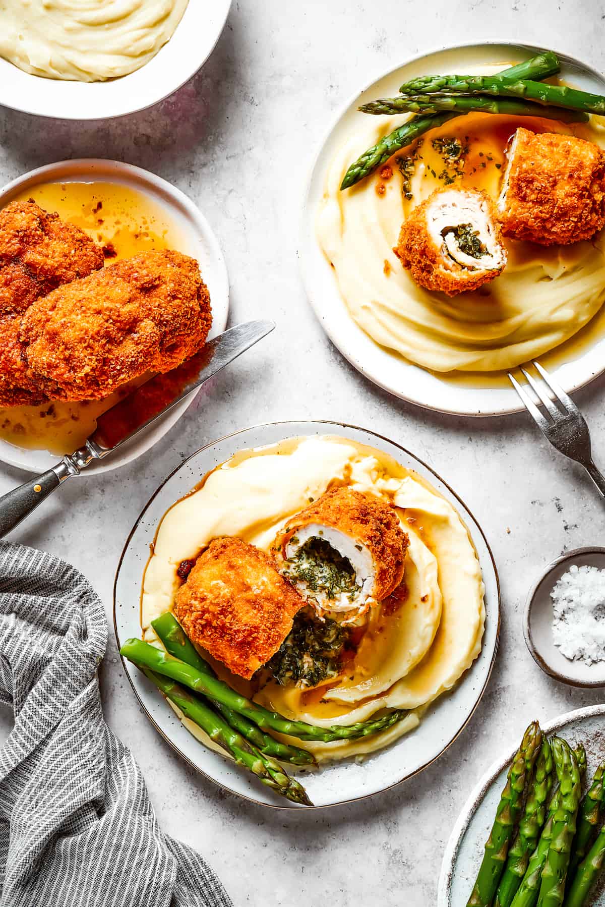 Chicken Kiev served on dinner plates with mashed potatoes and asparagus.