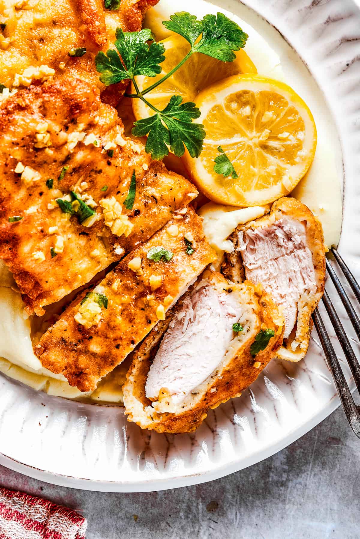 Sliced Breaded chicken with parsley and lemon slices placed next to it.