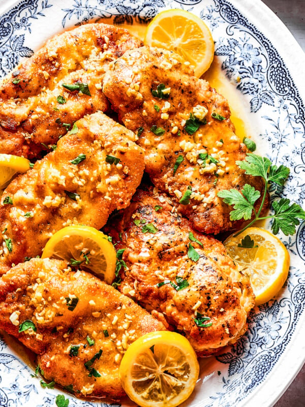 Homemade lemon chicken recipe arranged on a platter with parsley and lemon slices.