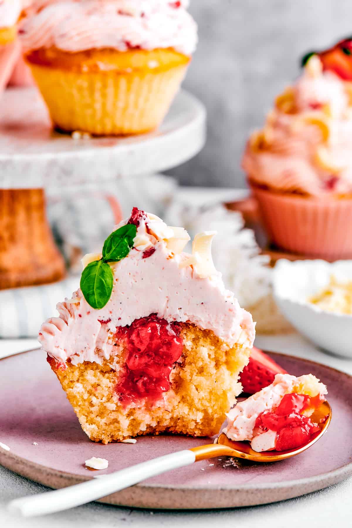 A strawberry cupcake set on a plate and cut in half to show the filling.