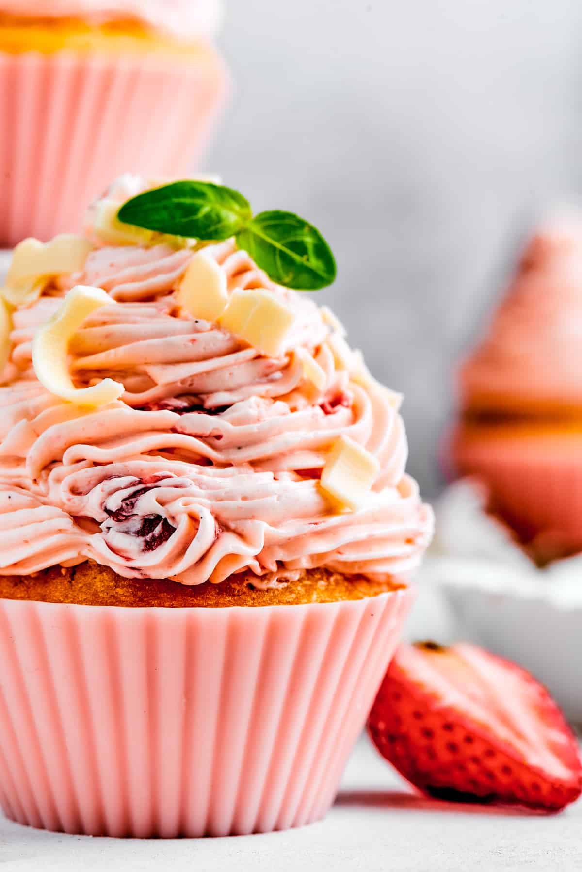 A strawberry cupcake garnished with mint and strawaberry.