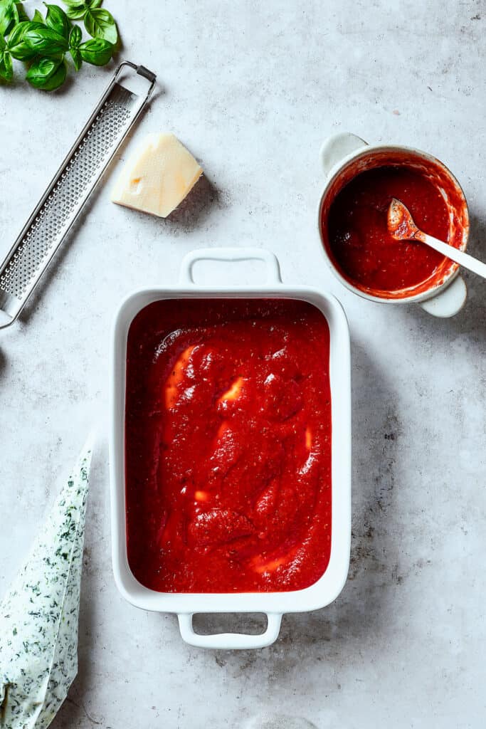 Red sauce spread into the bottom of a casserole.