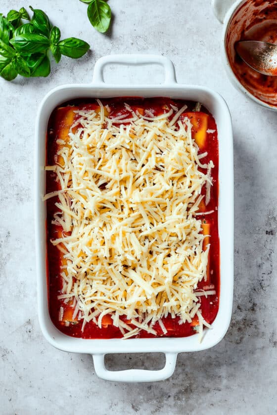 Pasta topped with sauce and shredded mozzarella in a baking dish.