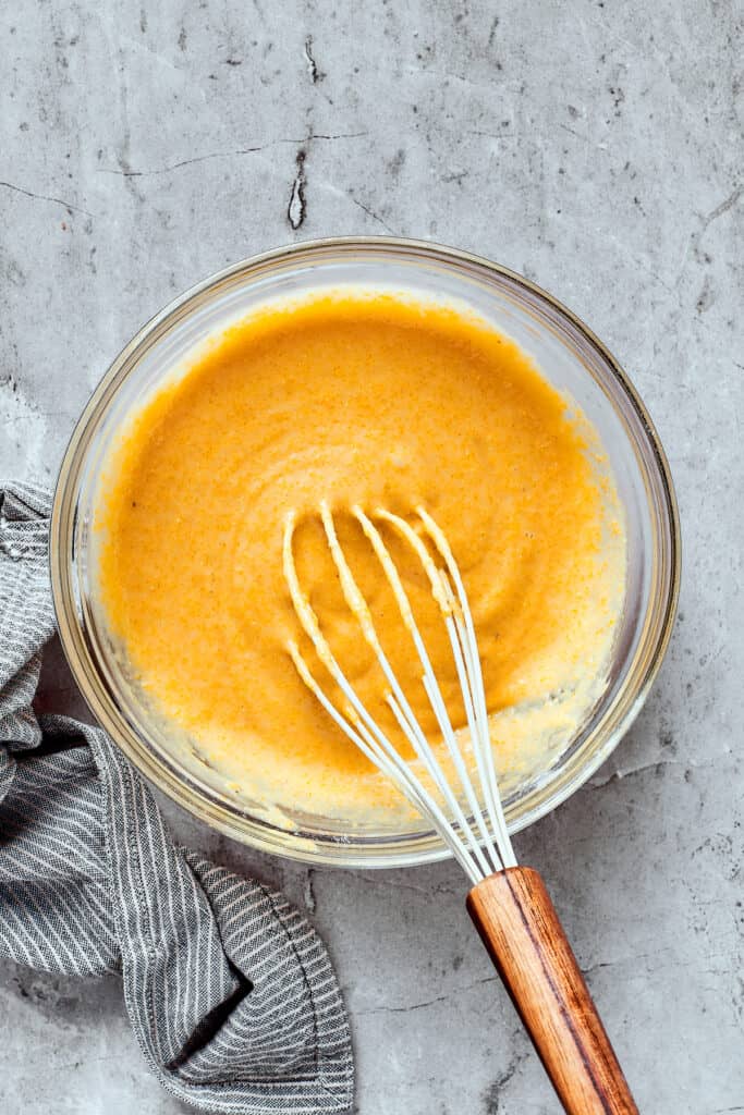 Yellow cornbread batter in a mixing bowl with a whisk.