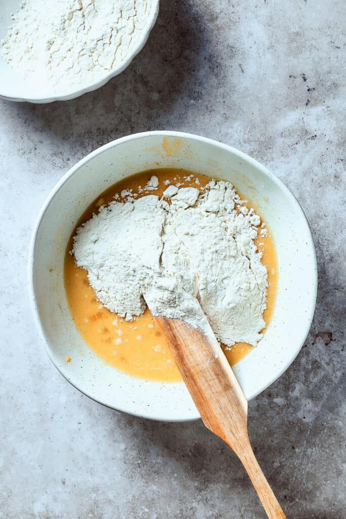 Adding flour to a bowl of dough ingredients.