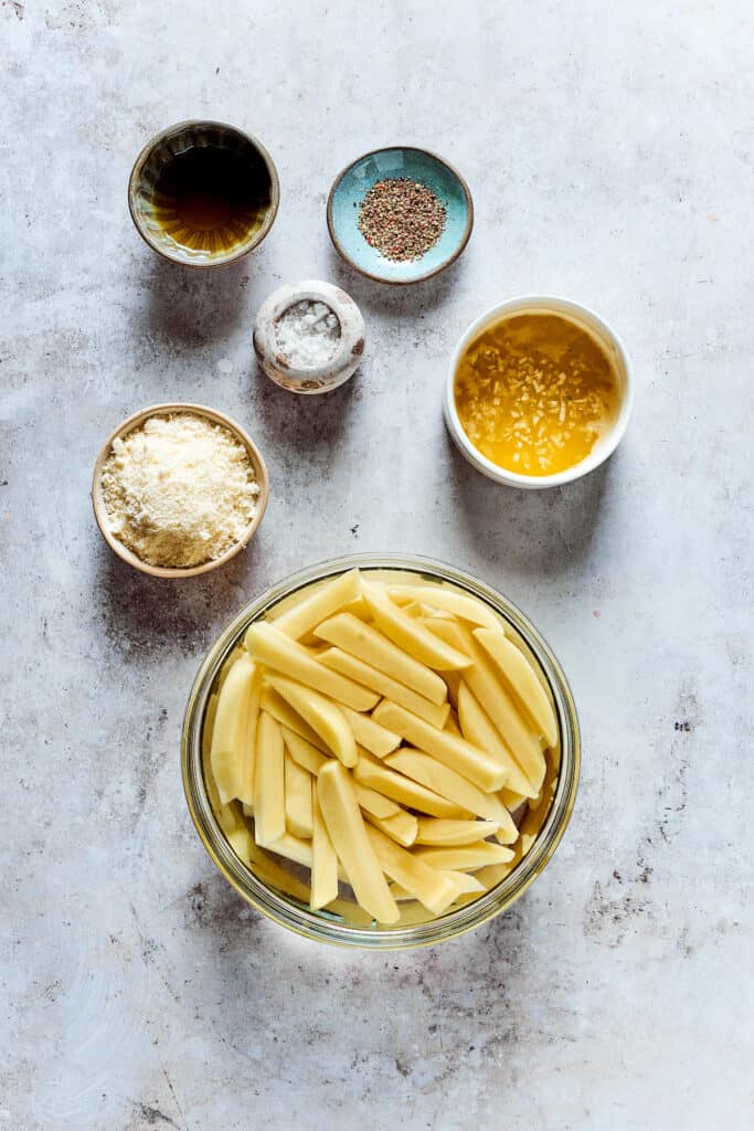 Cut fries soaking in water, with other ingredients in dishes on the work surface.