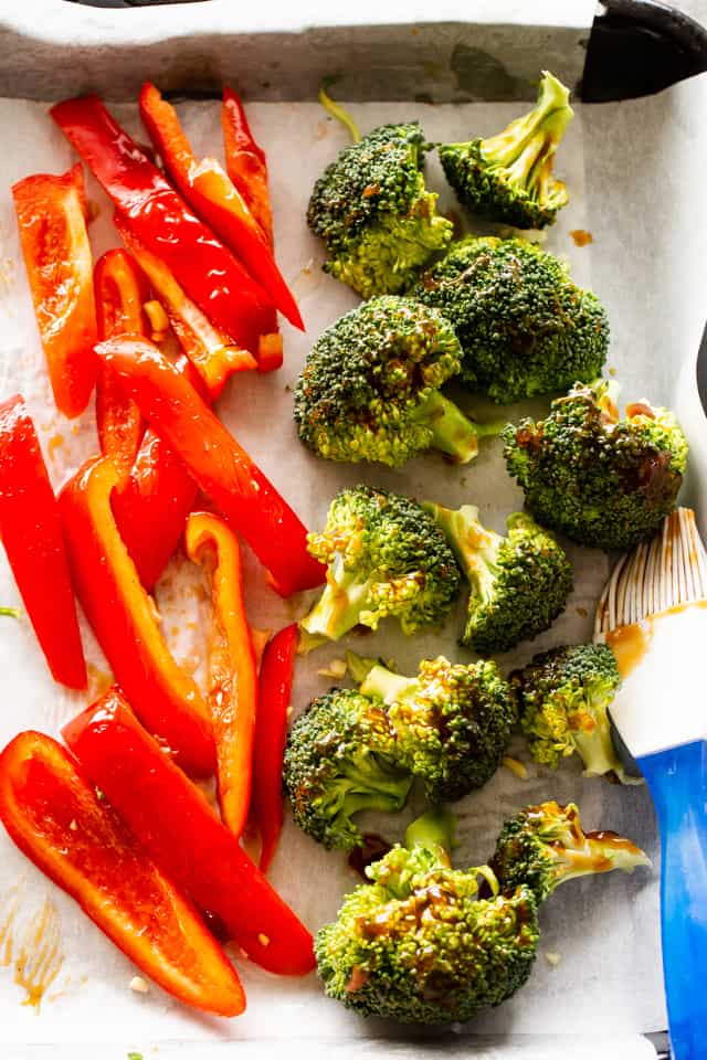 Red bell pepper slices and broccoli florets arranged on a baking sheet.