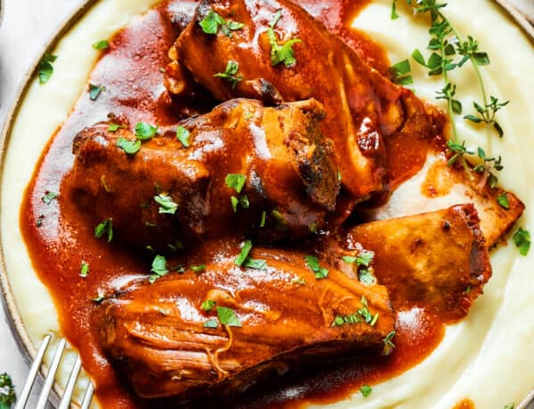 A bowl of mashed potatoes topped with ribs and sauce.