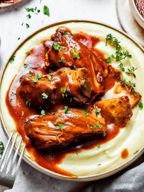 A bowl of mashed potatoes topped with ribs and sauce.