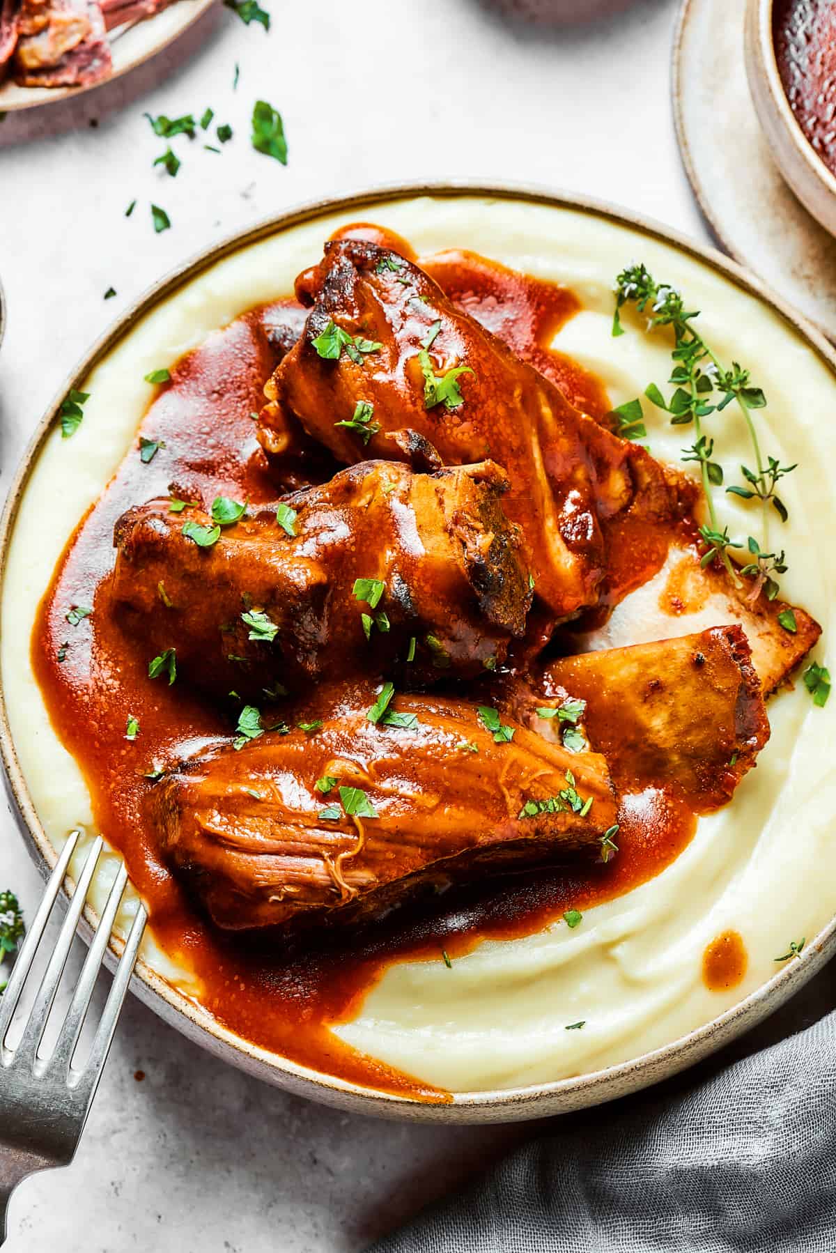 A bowl of mashed potatoes topped with ribs and sauce.