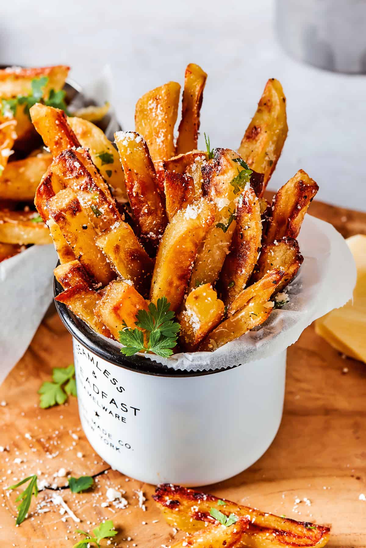 A serving of fries is stacked upright in a large white tin mug.