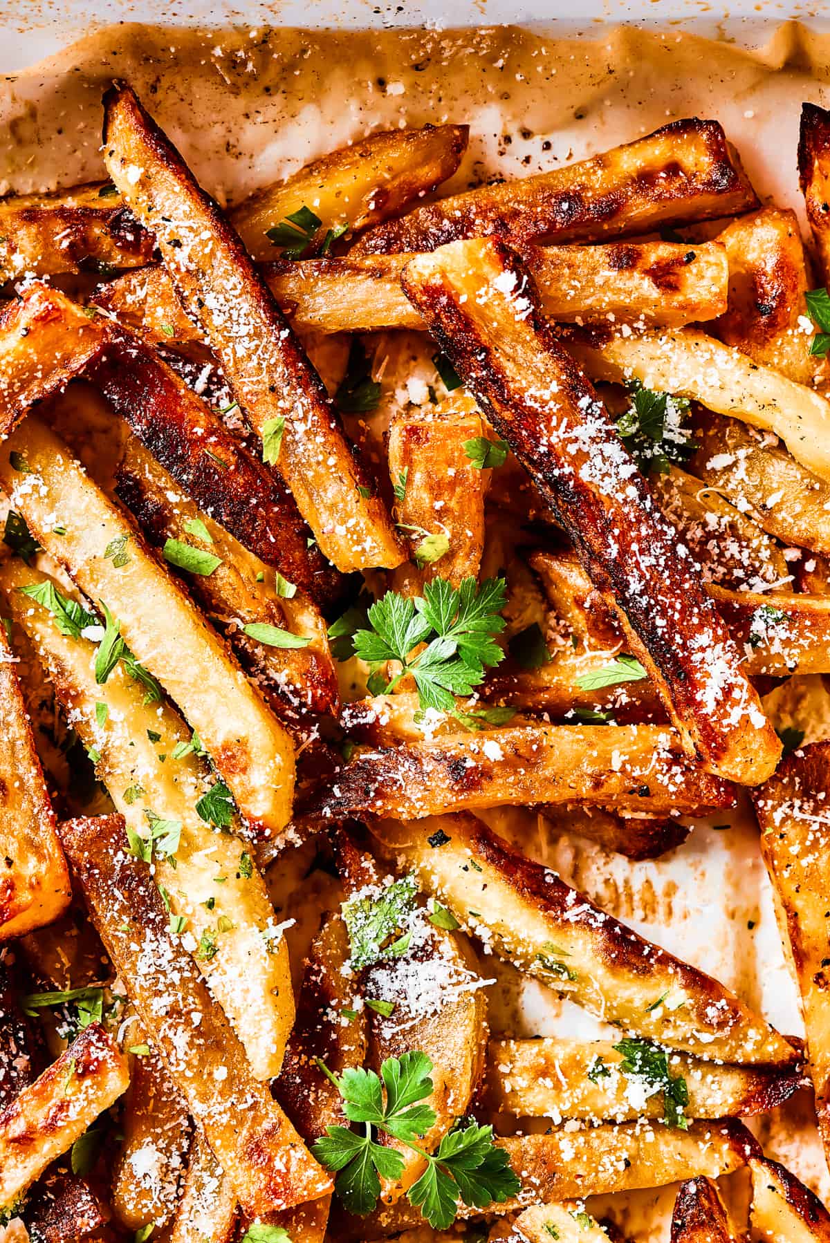 Close-up shot of seasoned garlic fries on a baking sheet and sprinkled with herbs and parmesan cheese.