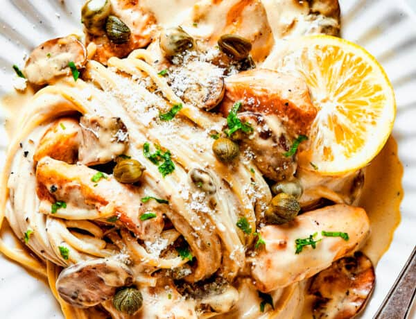 Chicken in caper-lemon sauce with pasta on a pale dinner plate.