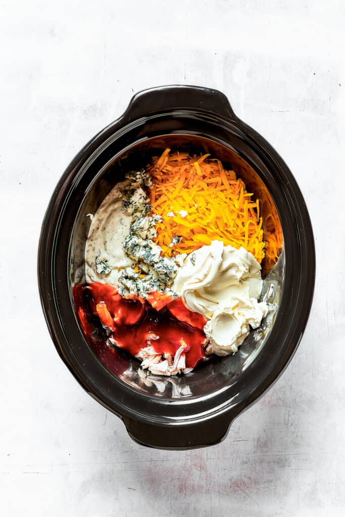 Cream cheese, blue cheese, chicken, and other ingredients in a slow cooker insert.