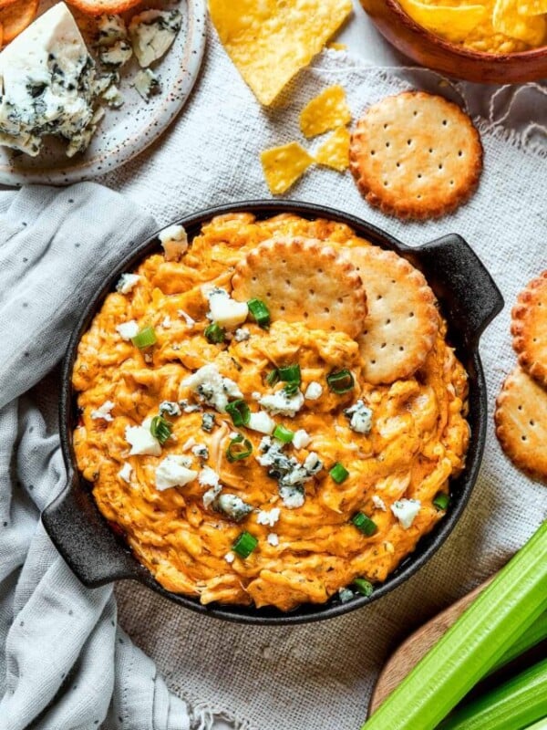 Overhead shot of a serving of buffalo dip with crackers, blue cheese, and green onions.