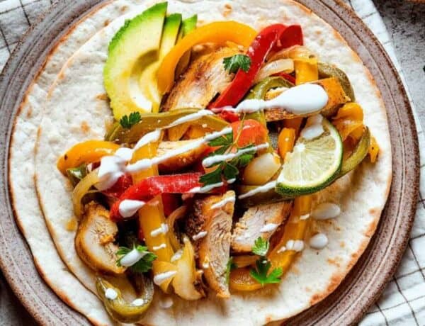 Crockpot chicken fajitas plated ad topped with lime, avocado, and sour cream.