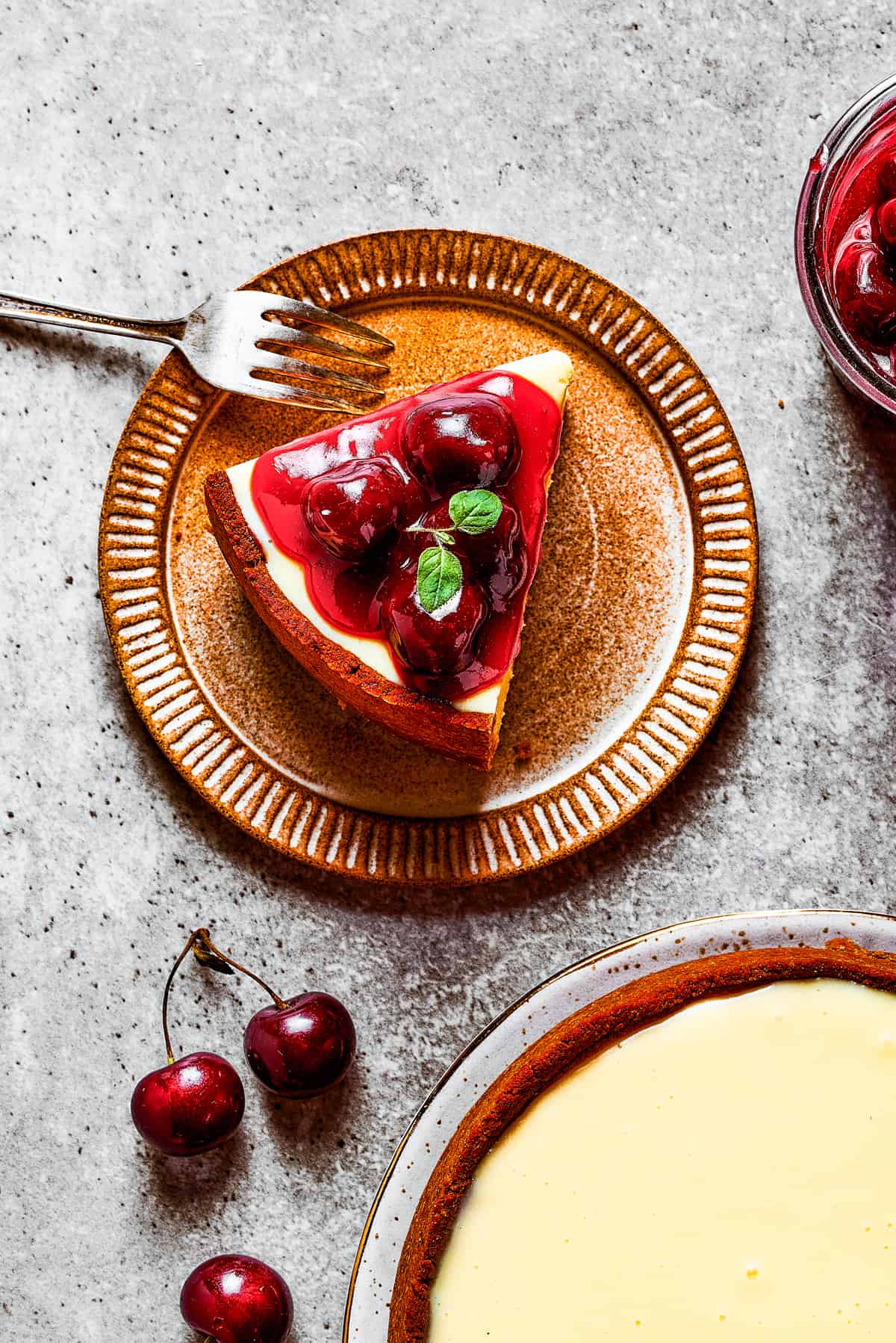 Overhead image of a slice of cheesecake topped with cherries and served on a dessert plate.