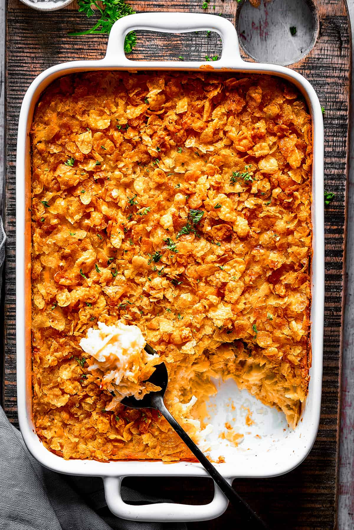 A baking dish with hashbrown casserole. Some of it has been spooned out, and a serving spoon is set on top of the casserole.