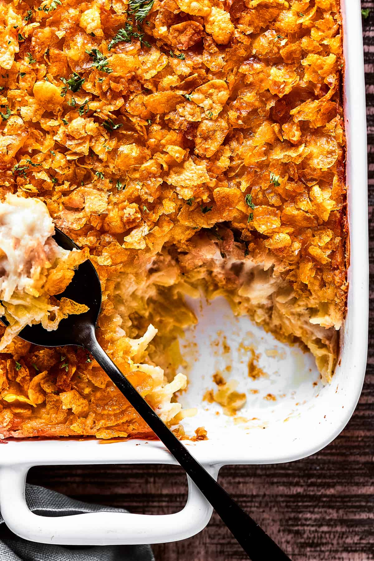 A white baking dish filled with hashbrown casserole. Some of it has been spooned out.