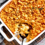 A casserole dish with hashbrown casserole. Some of it has been spooned out, and a serving spoon is set inside the casserole dish.