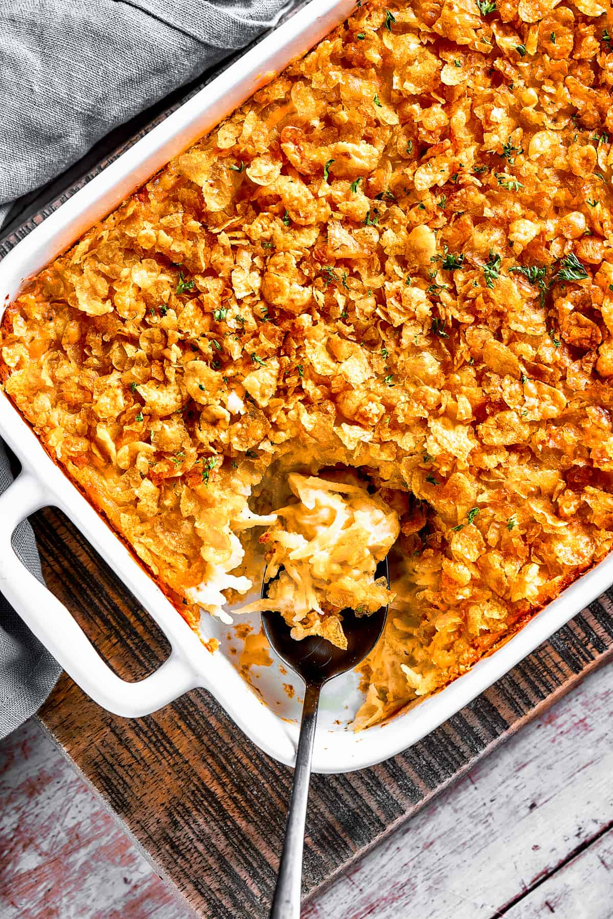 A casserole dish with hashbrown casserole. Some of it has been spooned out, and a serving spoon is set inside the casserole dish.