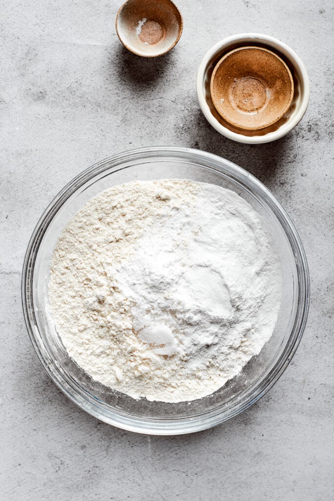 A mixing bowl full of a flour mixture, next to some small and empty bowls