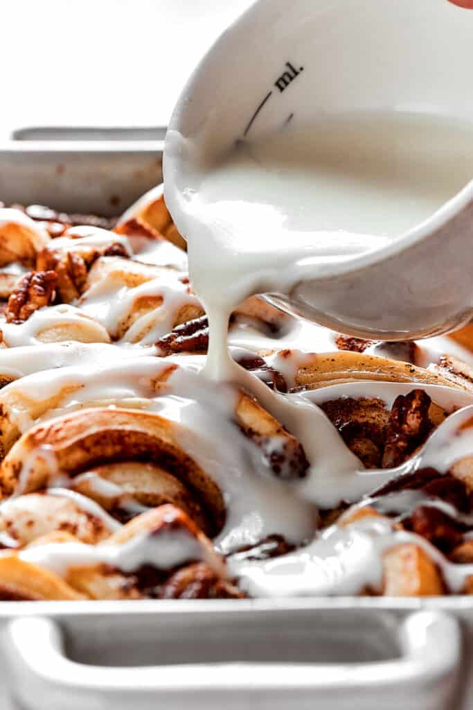 Close up of a bowl of icing being poured over cinnamon roll casserole