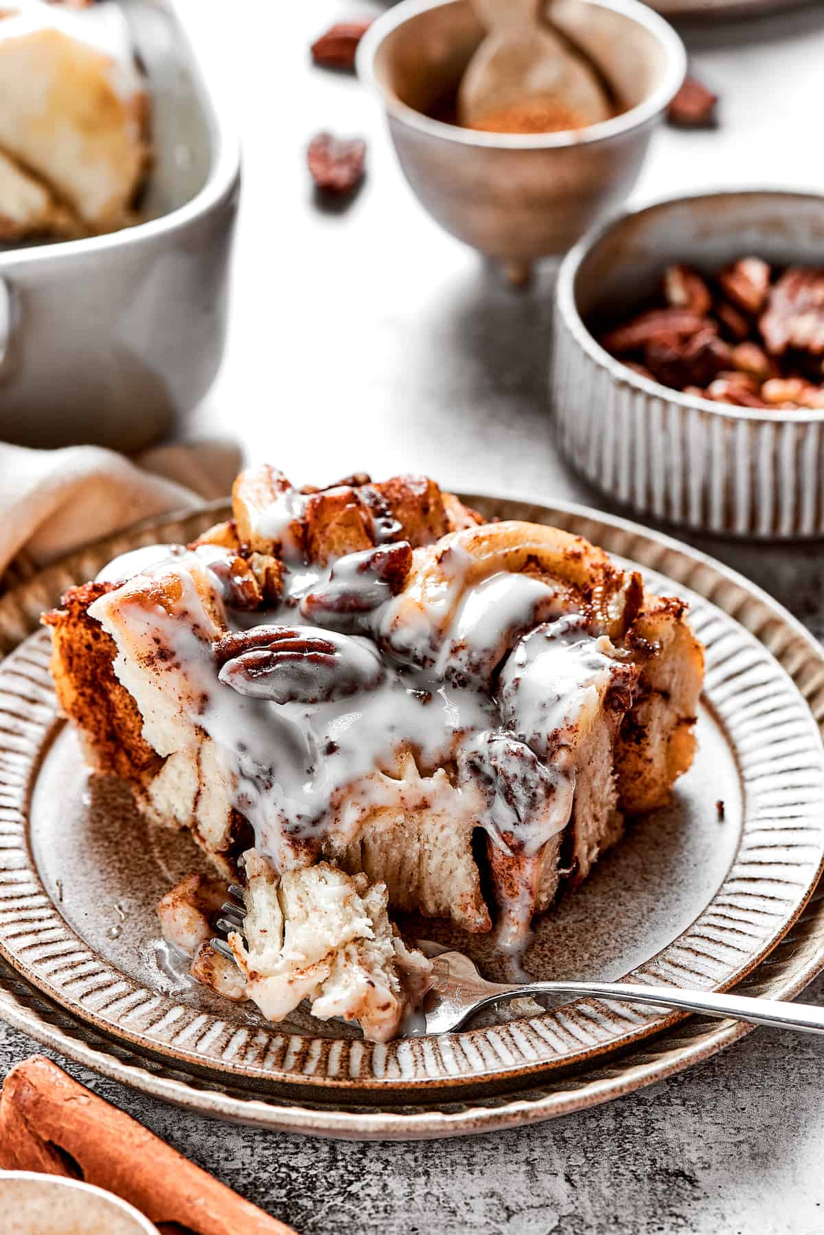 A square of cinnamon roll casserole on a plate with icing, with a fork taking a bit