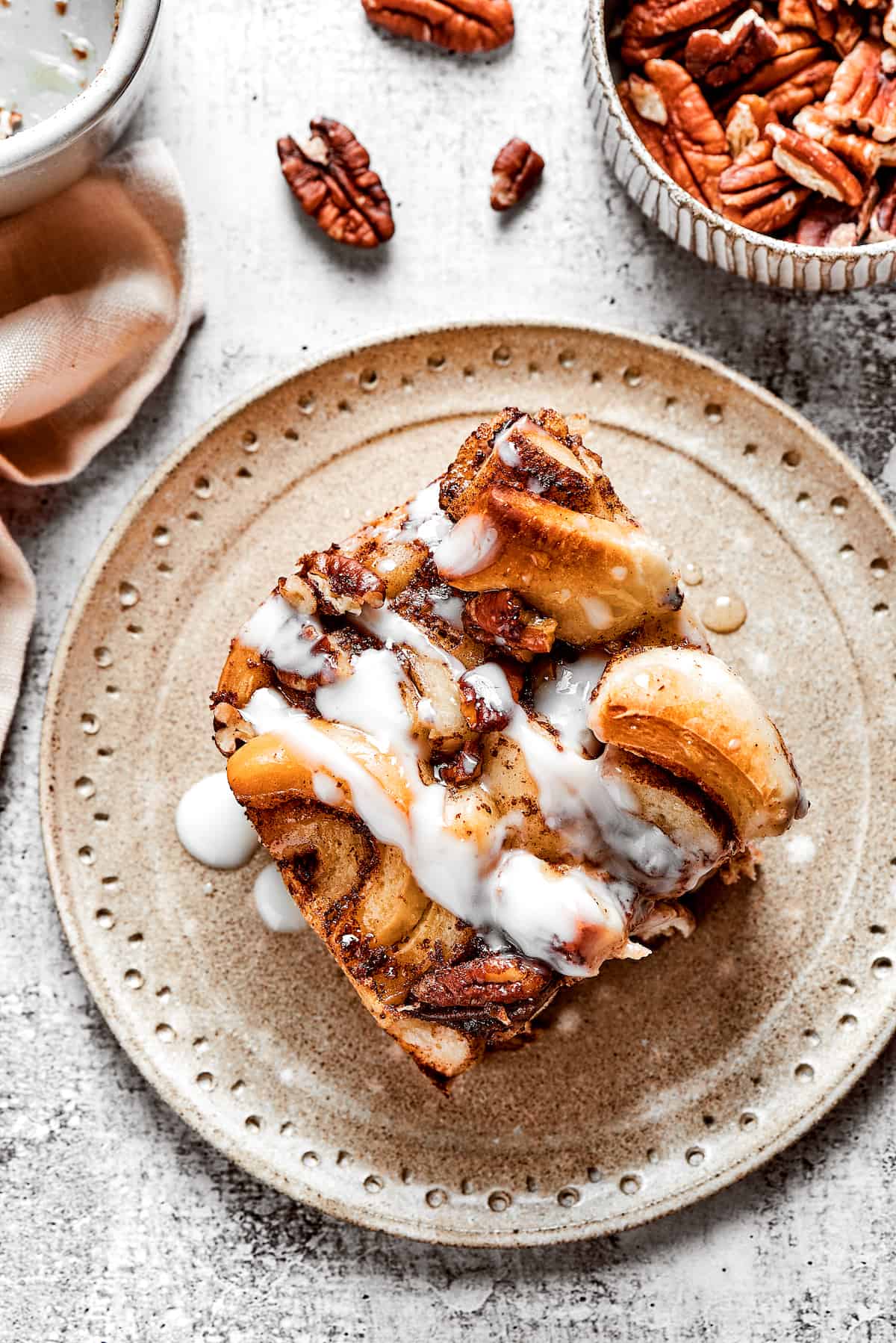 Overhead view of a slice of cinnamon roll casserole on a plate, next to a bowl of pecans