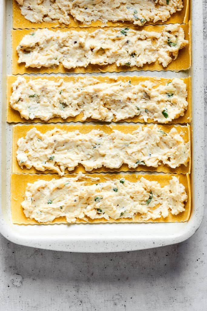 Overhead view of lasagna noodles with a cheese mixture spread over them.