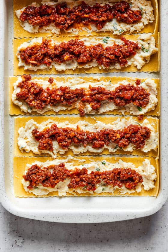 Overhead view of lasagna noodles covered with a cheese mixture and a ragu.