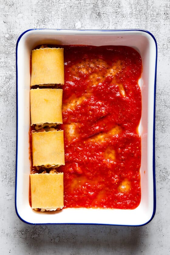 Overhead view of a baking dish partially filled with unbaked lasagna roll ups on top of marinara sauce.