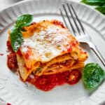 A lasagna roll on a plate with basil leaves and a fork.