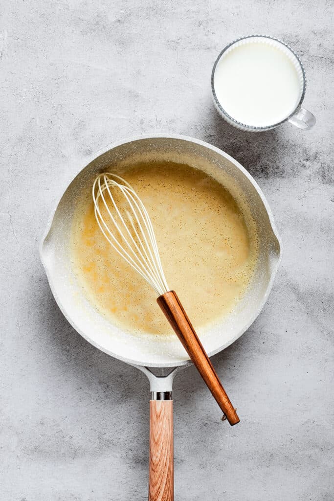 A saucepan filled with a roux and a whisk.