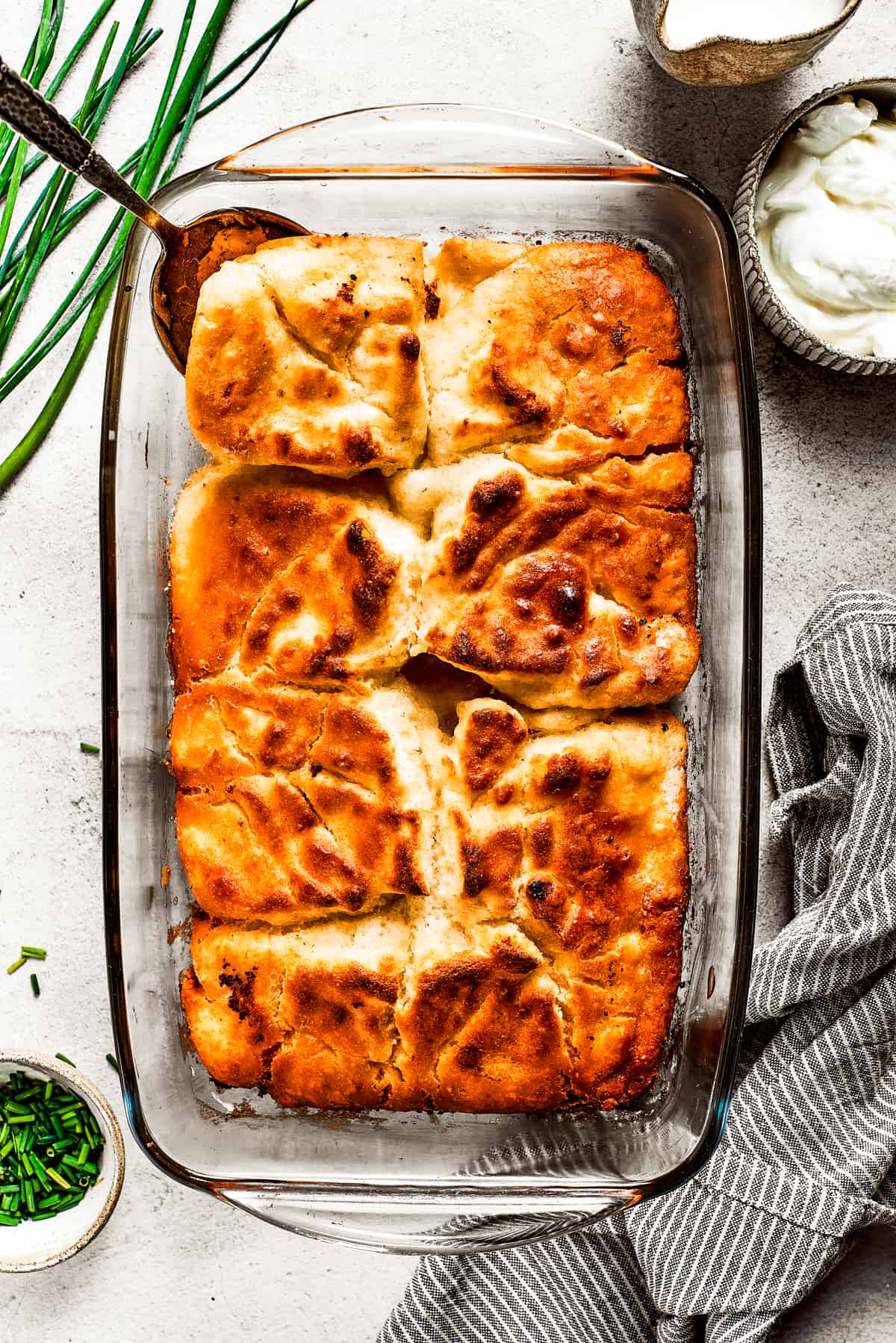 Overhead view of a baking dish full of butter swim biscuits, with a serving spoon removing a corner piece.