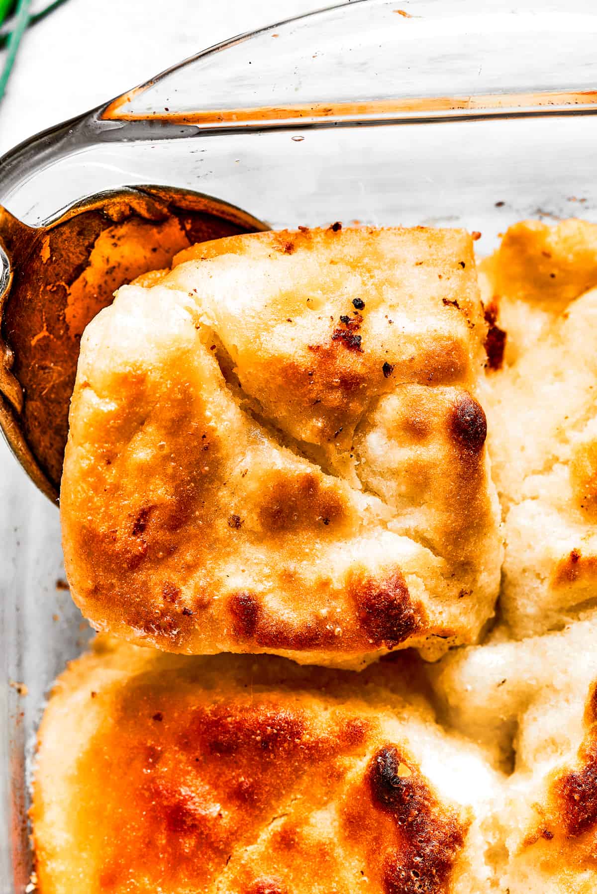 Close-up shot of a serving spoon removing a corner piece from a pan of biscuits.