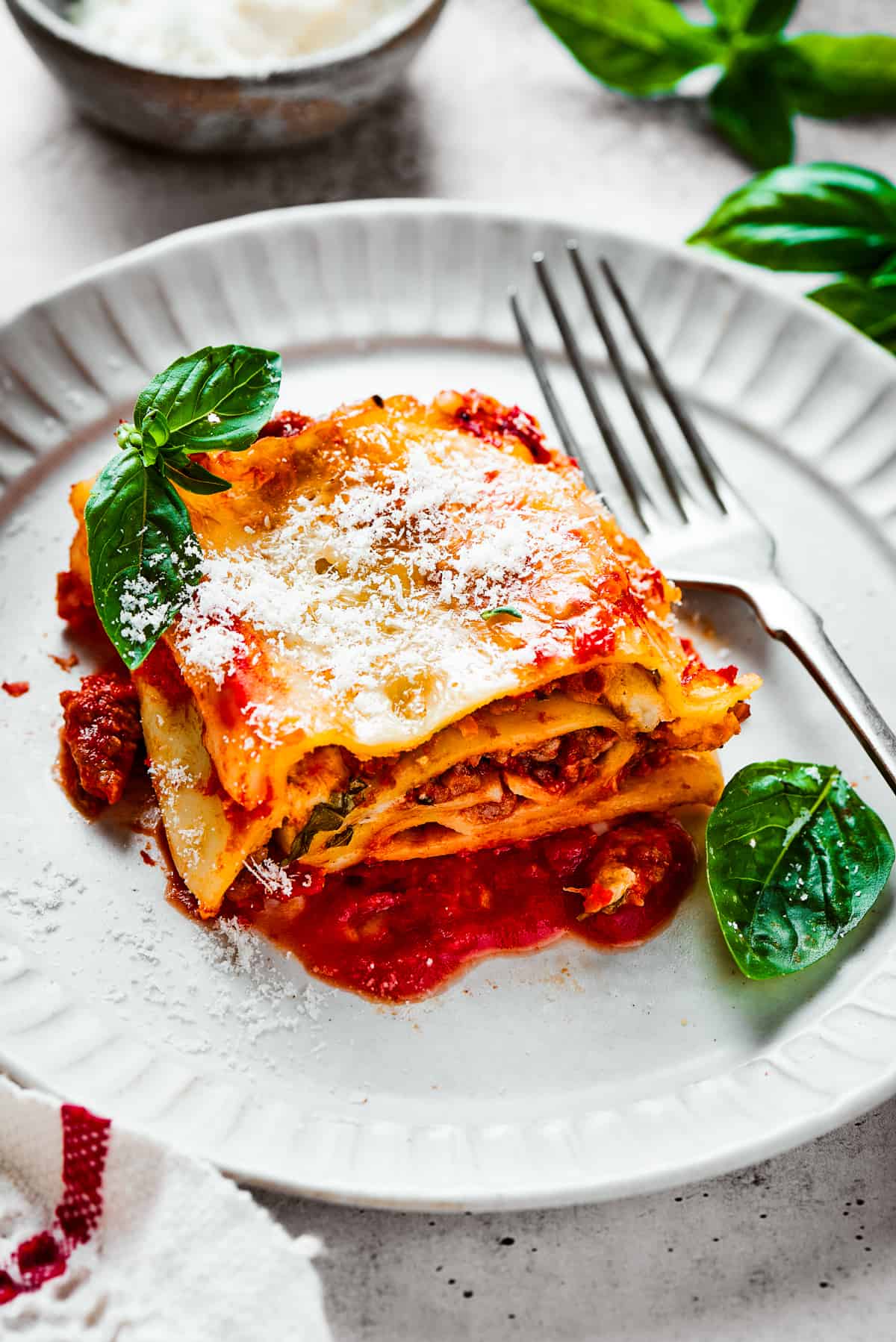 A lasagna roll on a plate with basil leaves and a fork.
