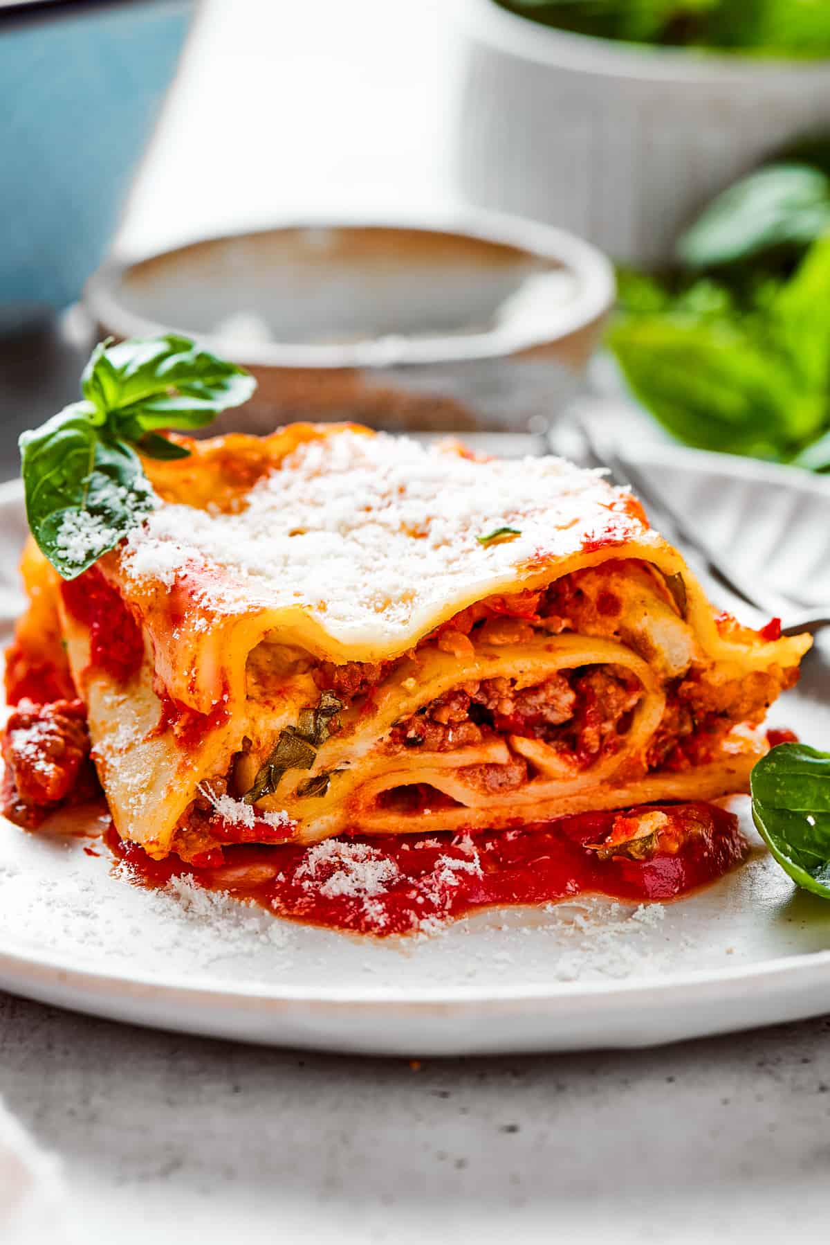 Lasagna roll up served on a white dinner plate and garnished with fresh basil leaves.