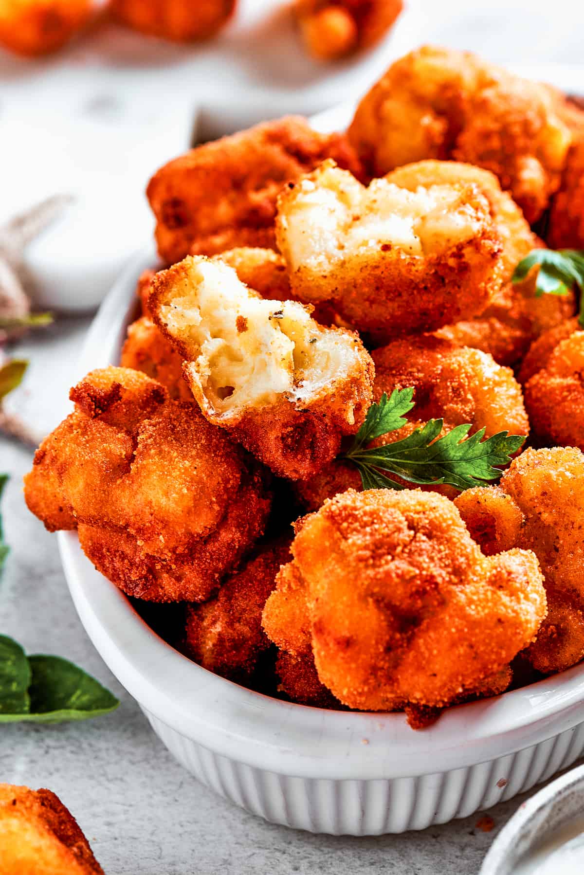 A serving bowl full of fried mac and cheese bites, surrounded by more mac and cheese balls.