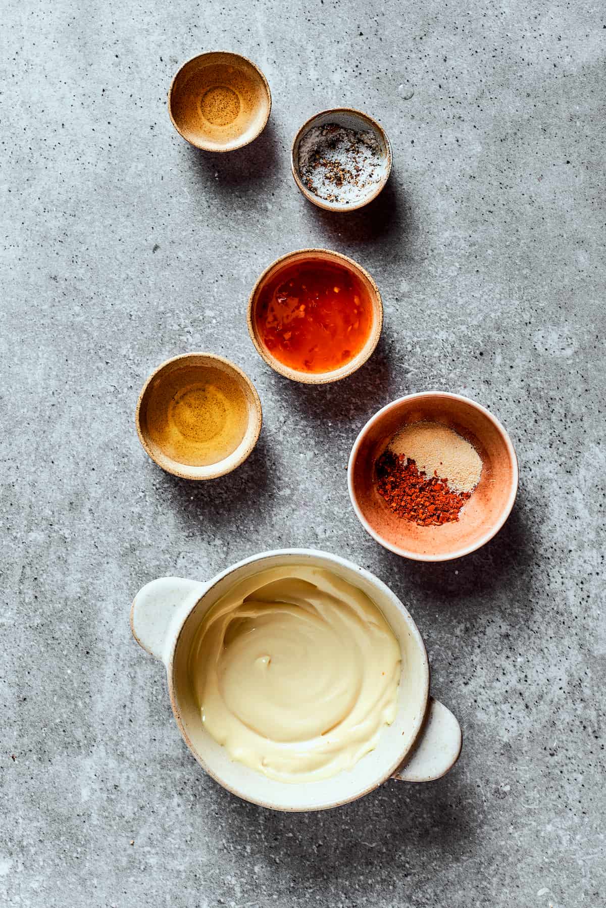 Overhead view of the ingredients needed for bang bang sauce: a bowl of mayonnaise, a bowl of sweet chili sauce, a bowl of honey, a bowl of rice vinegar, a bowl of salt and pepper, and a bowl of garlic powder and chili flakes.