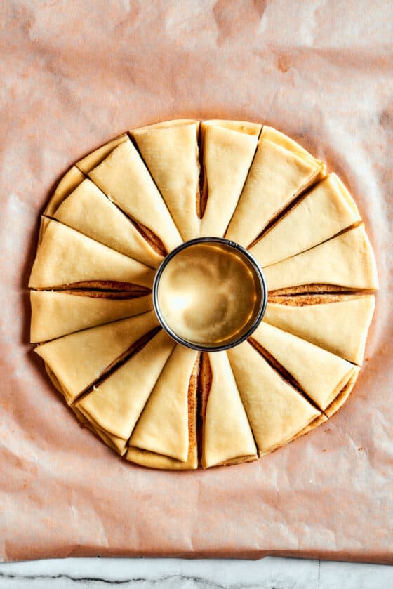 Overhead view of a star bread dough cut into 16 segments, with a glass in the middle.